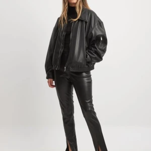 Svarta skinnbyxor med slits - Snygga svarta skinnbyxor med hög midja och slits vid bensluten. Byxorna har en tight passform och ger en cool look. Perfekta för att höja din stil till nästa nivå.