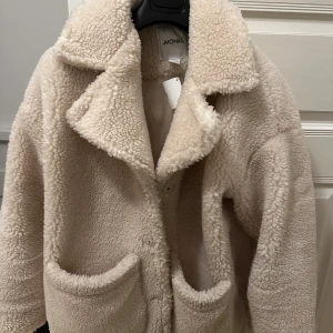Beige cremevit stor oversized teddyjacka från Monki - Mysig beige teddyjacka från Monki med stora fickor och en klassisk krage. Perfekt för kyliga dagar när du vill hålla dig varm och stilren. Jackan har en avslappnad passform och är knappt använd. 