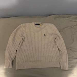 Beige kabelstickad tröja från Ralph Lauren st M - Säljer en stilren beige kabelstickad tröja från Ralph Lauren. Tröjan har en klassisk design med rund hals och det ikoniska logotypbroderiet på bröstet. Perfekt för en elegant och avslappnad look. Använd 2 gånger, säljs pga för liten. Pris kan diskuteras. Inte äkta.