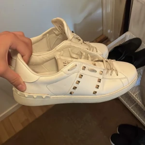Valentino open - Snygga vita sneakers från Valentino med ikoniska nitar på sidorna och hälen. Skorna har en klassisk design med snörning och är perfekta för en stilren look.Dom är i hyfsat skick och allt og finns ,Helt äkta såklart!!! Säljes för 2900