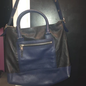 Svart och blå axelväska från Coach - Snygg axelväska från Coach i svart och blått skinn. Väskan har en praktisk dragkedja framtill.