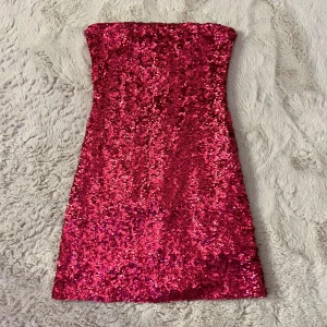 Röd/rosa paljettklänning från NA-KD - Snygg röd/rosa paljettklänning från NA-KD i en glittrig design. Klänningen är axelbandslös och har en dragkedja i ryggen för enkel påklädning. Perfekt för en festlig kväll! Kan både mötas upp i Stockholm och frakta!❤️💕