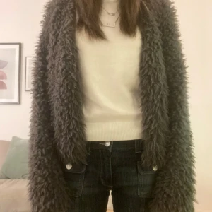 Grå teddyjacka från Gina Tricot - Mysig grå teddyjacka från Gina Tricot i storlek S. Perfekt för kyliga dagar med sin fluffiga och mjuka textur. Jackan har en öppen design utan knappar eller dragkedja, vilket ger en avslappnad look.