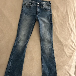 Blå bootcut jeans från H&M - Säljer ett par blå lågmidjade bootcut jeans från H&M med justerbar midja. Jeansen är använda endast 2 gånger och är i bra skick.😊