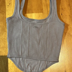 Lila ribbad linnetopp från Victoria's Secret PINK collection köpt från Turkiet  - Snygg grå ribbad träningstopp från Victoria's Secret PINK. Perfekt för en casual look med sin stilrena design och broderade logga framtill. Toppen har en bekväm passform och är tillverkad i mjukt material.