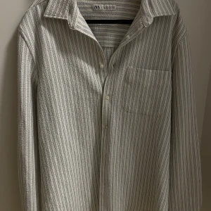 Randig skjorta från Zara - Snygg randig skjorta från Zara i vitt med tunna svarta ränder. Säljer denna fina tröja då den är för liten för mig. Storlek M. Köpt på Zara och är i väldigt fint skick. Hör av er om fler bilder eller frågor.