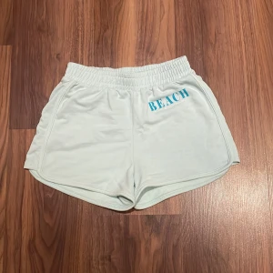 Ljusblå shorts från H&M - Säljer ett par ljusblå shorts från H&M med texten 'BEACH dreams' tryckt på framsidan. De har en elastisk midja för extra komfort. Perfekta för en dag på stranden eller en avslappnad sommarlook. Storlek 158