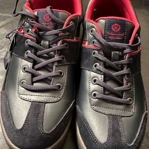 Snygga mörkblå sneakers från Henri Lloyd  - Snygga mörkblå sneakers från Henri Lloyd med röda och gula detaljer. Skorna har en klassisk snörning och en bekväm gummisula. Perfekta för en stilren look.