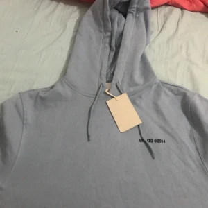 Grå hoodie från Axel Arigato - Snygg grå hoodie från Axel Arigato med tryck på både fram- och baksidan. Perfekt för en stilren och avslappnad look. Huvan har dragsko för justerbar passform.