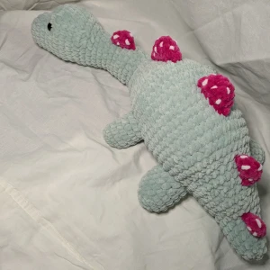 Jordgubbs dino🦕 - En egenvirkad stor dino som är gjord av 100% polyester och har säkerhetsögon. Den är gosig och perfekt till barn. Längd: 47 cm, höjd: 17 cm, bred: 23 cm