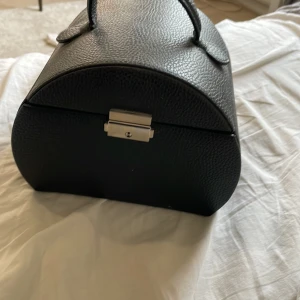 Svart smyckeskrin med spegel - Elegant svart smyckeskrin med en praktisk spegel inuti. Skrinet har flera fack för att organisera smycken och en sektion för ringar. Perfekt för att hålla ordning på dina accessoarer.