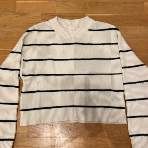 Vit och svart randig tröja från Zara - Säljer en snygg vit tröja från Zara med svarta ränder. Tröjan är ribbad och har en croppad passform med långa ärmar. Perfekt för en stilren look!