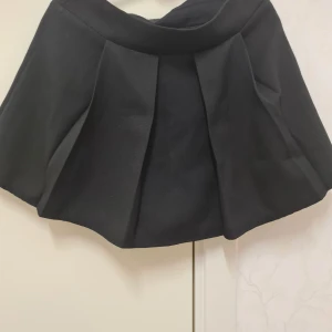 Svart kjol med shorts - Kort svart kjol med shorts och veckade detaljer. Har nu vuxit ur den. Finns dragkedja  på sidan för att tas på/av.