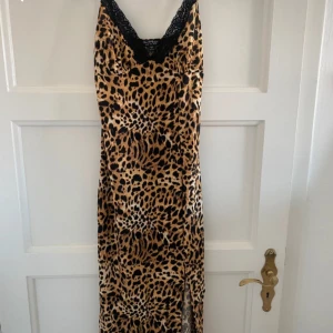 Leopardmönstrad klänning från Miss Selfridge - Snygg leopardmönstrad långklänning från Miss Selfridge med spetsdetaljer vid halsringningen. Klänningen har en slits som ger en extra touch av stil. Perfekt för en djärv look!