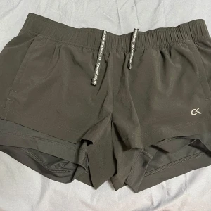 Calvin Klein träningsshorts - Fina och sparsamt använda svarta träningsshorts från Calvin Klein. Har både innershorts och fickor. Lappen är tyvärr bortklippt men uppskattar att de är i storlek M. Är inte jättetighta, och kan knytas åt i midjan med snörena. 