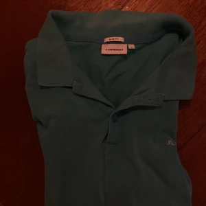 Pikétröja från J.Lindeberg - Säljer en stilren blå pikétröja från J.Lindeberg i storlek L. Tröjan är tillverkad i 100% bomull och har en slim fit passform. Hör av dig om du har några frågor. 