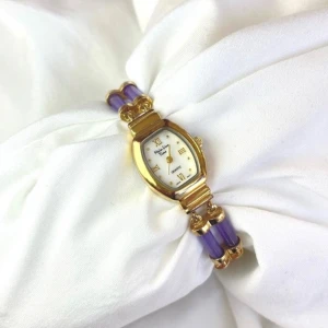 Färgglad vintage klocka  - Snygg klocka från Calypso Studios med ett armband i lila, grönt och rött. Klockan är i guld och urtavlan är vit med romerska siffror. Säljer eftersom den jag behöll är väldigt lik :)