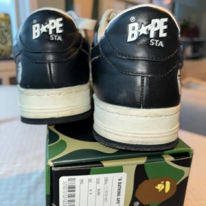 Svartvita sneakers från BAPE - Snygga BAPE STA sneakers i svart och vitt med den ikoniska stjärndesignen på sidan. Skorna har snörning och en robust sula, perfekt för en streetwear-look. De kommer i originalförpackning med det klassiska kamouflagemönstret.