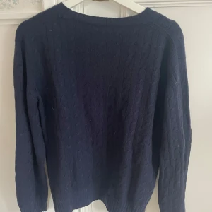 Mörkblå stickad tröja - Säljer en stilren mörkblå stickad tröja med rund halsringning. Tröjan har långa ärmar och ett diskret kabelstickat mönster som ger en klassisk look. Perfekt för kyligare dagar.