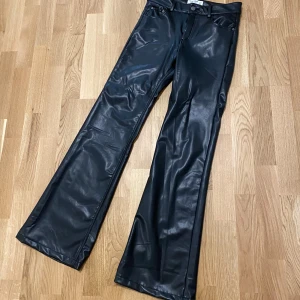Svarta skinnbyxor från Pull&Bear  opium core vamp  - Snygga svarta skinnbyxor från Pull&Bear med en modern bootcut-stil. Byxorna har en hög midja och stängs med dragkedja och knapp. Perfekta för en trendig look.