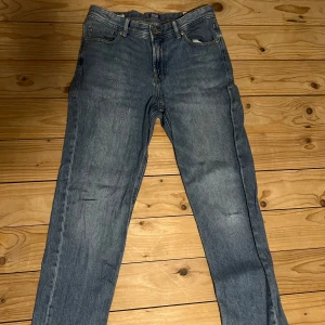 Blå jeans från Jack & Jones - Säljer ett par klassiska blå jeans från Jack & Jones i modellen Regular Clark. Perfekta för en avslappnad stil med en bekväm passform. De har en traditionell femficksdesign och knappgylf. Den har hål på ena knäet men har för mig att det är design.