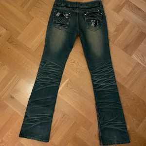 Bootcut jeans med snygga detaljer - Snygga vintage bootcut jeans med unika detaljer på bakfickorna. Storlek 27 och är något små i storleken, men stretchiga! Skriv för fler bilder, hur de sitter på osv..