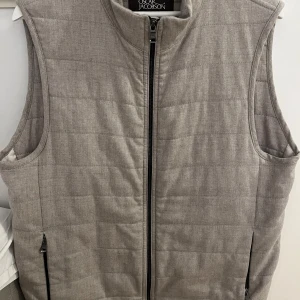 Grå quiltad väst från Oscar Jacobson - Snygg grå quiltad väst från Oscar Jacobson med dragkedja framtill. Perfekt för lager-på-lager under kyliga dagar. Västen har en stilren design med praktiska fickor. Modellen är 192. Storlek 52. Nypris 3000kr