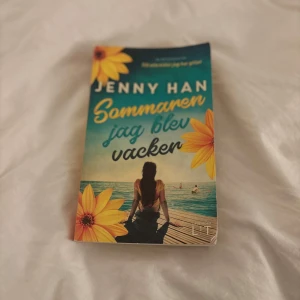 Sommaren jag blev vacker - En bok av Jenny Han med titeln 'Sommaren jag blev vacker'. Omslaget visar en person vid en brygga med solrosor i hörnen, vilket ger en somrig känsla. Perfekt för dig som gillar romantiska och känslosamma berättelser.Personligen tycker jag att boken är väldigt bra och spännande!