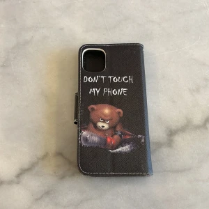 Svart mobilfodral med björntryck till iPhone 11 - Snyggt svart mobilfodral med ett tufft tryck av en björn som håller i en motorsåg och texten 'Don't touch my phone'. Perfekt för att skydda din telefon med stil. Alla telefon skal är till iphone 11