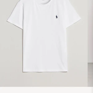 Vit t-shirt från Polo Ralph Lauren - Säljer en klassisk vit t-shirt från Polo Ralph Lauren med det ikoniska broderade logotypen i blått på bröstet. Perfekt basplagg för alla tillfällen.