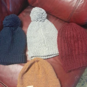 Fyra stickade mössor i olika färger 25 kr  styck  - Säljer ett set med fyra stickade mössor i olika färger: marinblå, ljusgrå, brun och vinröd. Två av mössorna har en stor tofs på toppen för extra stil. Perfekta för att hålla dig varm under kalla dagar!