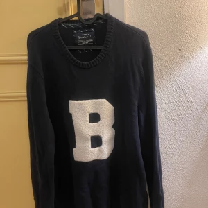 Mörkblå tröja med bokstaven B - Snygg mörkblå tröja  med en stor vit bokstav B på framsidan. Tröjan har långa ärmar och en rund halsringning. Perfekt för en avslappnad stil.