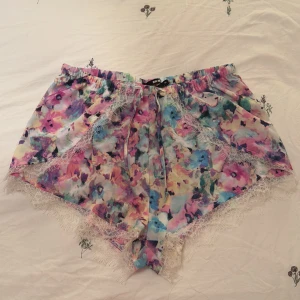 Blommiga shorts med spetsdetaljer - Färgglada blommiga sommar shorts med spetsdetaljer. Sparsamt använda. Kan även använda som pyjamas. 
