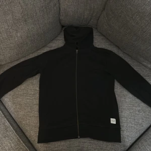 Svart hoodie från Jack & Jones - Säljer en stilren svart hoodie från Jack & Jones Essentials. Den har en dragkedja framtill och en praktisk huva. Perfekt för en avslappnad look.