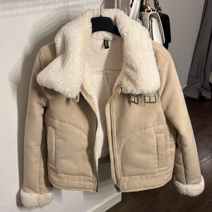 Beige teddyjacka från H&M - Säljer en mysig beige teddyjacka från H&M med fluffigt foder och krage. Jackan har dragkedja och spännen vid kragen för extra stil. Denna jacka är knappt använd, vilket är därför jag säljer den. Jackan finns inte längre i butik💕