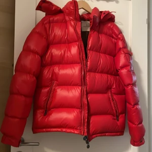 Röd dunjacka från Moncler - Snygg röd dunjacka från Moncler med dragkedja och huva. Jackan har en quiltad design och praktiska fickor med dragkedja. Perfekt för kyliga dagar med stil. Jag fick jackan i present och jag har använt en vinter och vill sälja den då de inte är min stil. Vill bara bli av med den. Den tar plats.