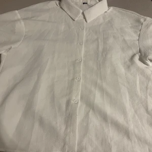 Vit skjorta med knappar från Shein - Snygg vit skjorta med klassisk krage och knappar framtill. Perfekt för en stilren look. Skjortan har korta ärmar och är tillverkad i ett lätt material.