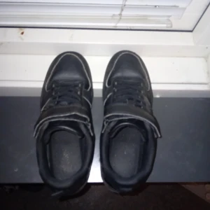 Svarta sneakers med snörning - Säljer ett par svarta sneakers med snörning och kardborreband. Skorna har en robust sula och är tillverkade i syntetmaterial. Perfekta för vardagsbruk.