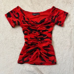 Röd och svart camouflage mönstrad topp - Snygg röd topp med svart kamouflagemönster. Den har en åtsittande passform och korta ärmar. Oanvänd i jättebra skick strl XS.