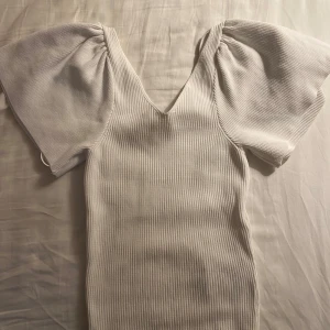 Vit ribbad topp - Säljer en stilren vit ribbad topp med korta puffärmar och v-ringning. Perfekt för en chic och enkel look.