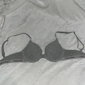 Grå bh från Calvin Klein - Säljer en grå bh från Calvin Klein med märkets logga på resåren. Bh:n har justerbara axelband och en mjuk, bekväm passform. Perfekt för vardagsbruk. 