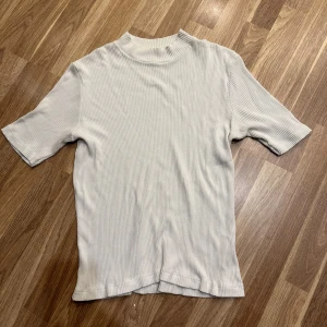 Vit ribbad topp - En stilren vit ribbad topp med en kort turtleneck med korta ärmar i storlek 46! Oanvänd! 