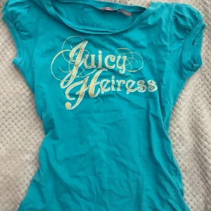 Turkos t-shirt från Juicy Couture - Snygg turkos t-shirt från Juicy Couture med texten 'Juicy Heiress' i glittriga bokstäver på framsidan. Den har korta ärmar och en rund halsringning.💗💗