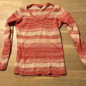 Randig stickad tröja från Indiska  - Säljer en snygg randig stickad tröja från Indiska i rosa, röd och beige. Tröjan har en v-ringad hals och långa ärmar, perfekt för kyligare dagar. Den är i storlek S och har en bekväm passform.