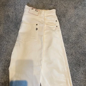 Vita dondup jeans  - Snygga vita jeans från Dondup med klassisk femficksdesign och knappgylf. De har en stilren look med subtila detaljer som märkeslogga på bakfickan. Perfekta för en fräsch och modern stil. Dom är i storlek w32-31 och passar dig som är runt 170 