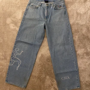 Jeans Cava Company - Snygga ljusblå jeansbyxor från Cava Company med unikt broderi på benet och en liten logga på fickan. Byxorna har en klassisk femficksdesign och knappgylf. Perfekta för en avslappnad stil.