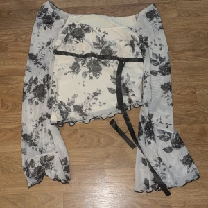 Blommig offshoulder blus med knytband - Snygg blommig offshoulder blus i svart och vit med långa ärmar och knytband i midjan. Perfekt för en stilren look 