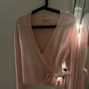 Rosa omlottkofta  - Säljer en söt rosa omlottkofta från Gina tricot. Koftan har en knytning i sidan och är långärmad med en mjuk och fluffig känsla. Använd endast en gång och har inga defekter. 