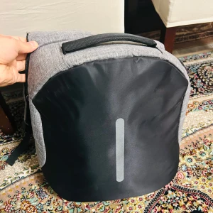 Grå och svart ryggsäck - Snygg och praktisk ryggsäck i grått och svart med en reflekterande detalj på framsidan. Den har vadderade axelremmar för extra komfort och ett rymligt huvudfack med dragkedja. Perfekt för vardagsbruk eller resor.