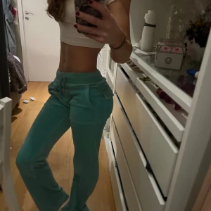 Turkosa mjukisbyxor från Juicy Couture - Säljer ett par snygga turkosa mjukisbyxor från Juicy Couture. Byxorna har en tight passform och är perfekta för en avslappnad stil. De har fickor med knappar bak och en bekväm midja.